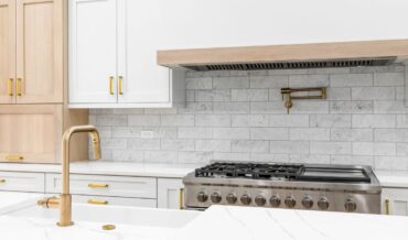 Discover a modern kitchen featuring innovative backsplash ideas with marble designs, complemented by white cabinets and gold fixtures. Enjoy cooking on the gas stove beneath a sleek built-in hood for a perfect blend of style and functionality.