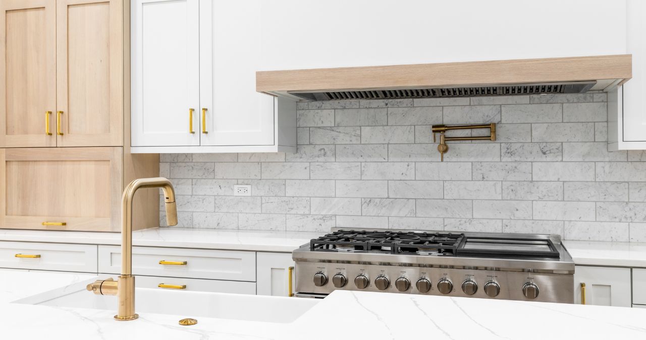 Discover a modern kitchen featuring innovative backsplash ideas with marble designs, complemented by white cabinets and gold fixtures. Enjoy cooking on the gas stove beneath a sleek built-in hood for a perfect blend of style and functionality.