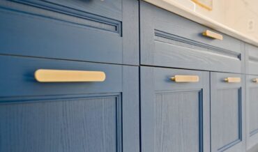 Close-up of blue kitchen cabinets with gold handles and a sleek white countertop above. Consider replacing cabinet door fronts for an easy refresh while maintaining this stunning color contrast.