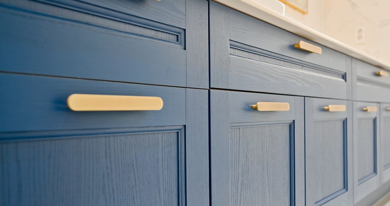 Close-up of blue kitchen cabinets with gold handles and a sleek white countertop above. Consider replacing cabinet door fronts for an easy refresh while maintaining this stunning color contrast.